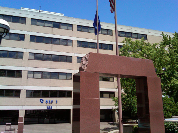 A front view of the State Education Building with its name GEF3 & #125 on it; An entrance structure and US flag beside in view. 