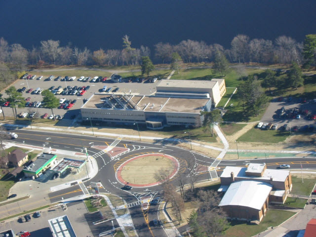 An aerial view of the Wisconsin Rapids State Office Building, parked cars, lakeview and lots of trees in the background.
